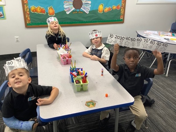 FAITH Academy students at a classroom table wearing counting-by-tens paper crowns